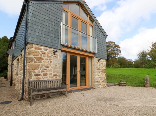Exterior view of a stone and wood house with a bench and gravel area in front at The Orchard in Cardinham