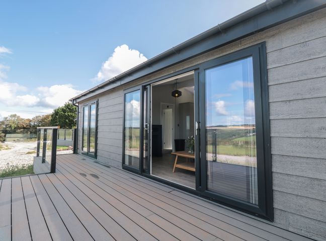 A terrace with glass railing and sliding doors leading to a room at Buttercup Lodge in Norton near Dartmouth