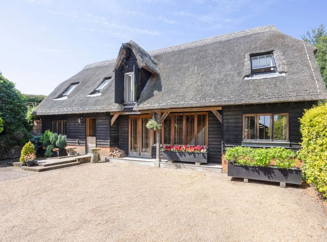 Exterior of a house with thatched roof flower boxes and gravel driveway at The Hayloft in Chislet near Herne Bay
