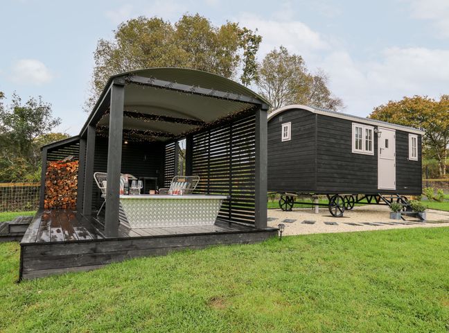 A black wooden shepherds hut on wheels with a covered wooden deck featuring a metal bathtub and chairs at Dragonfly Shepherd's Hut in Oakford near Aberaeron