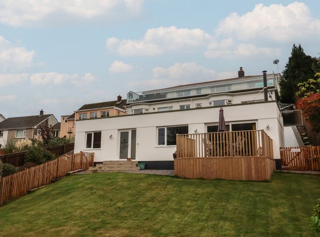 A white house with a wooden deck and green lawn at Robins Downs in Ilfracombe