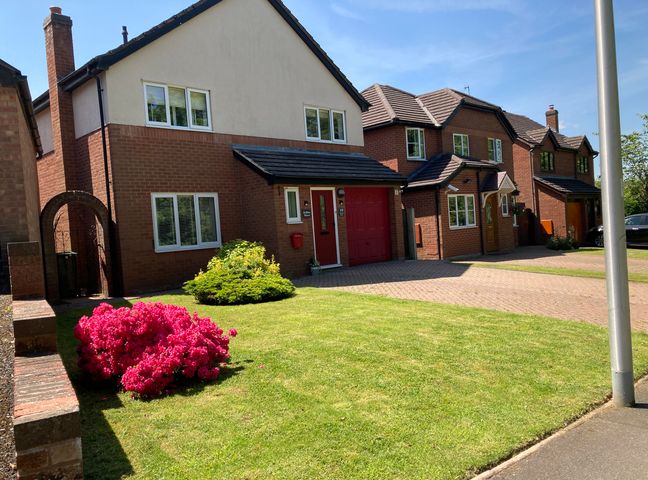 A row of brick houses with front lawns and a flowering shrub at Ludlow House in Ludlow