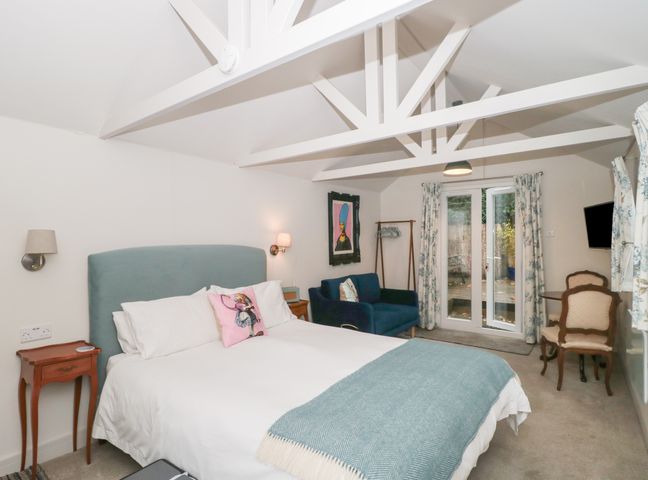 A bedroom with a bed a blue headboard a blue sofa chairs and a small table at The Potting Shed in Combe near Langport
