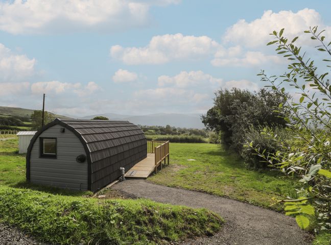 A small curved roof cabin on a grassy field with trees and hills in the background at Tarrenhendre Pod Llanegryn near Tywyn
