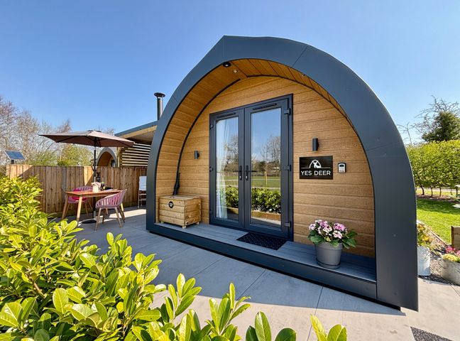 A wooden pod with curved roof patio table with umbrella and chairs outside at Yes Deer in Ashbourne