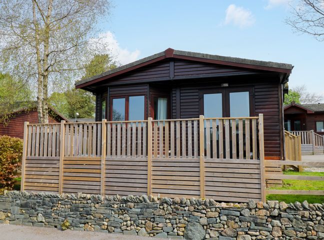 A wooden cabin with a fenced porch and stone wall in front at Hill Lodge in Applethwaite 2 Limefitt Park near Windermere