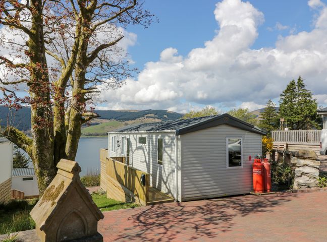 A static caravan with two red gas cylinders outside near a large tree and a lake in the background at 11A Mansion View in Cove near Kilcreggan