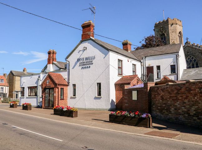 A white building with red brick chimneys and flower planters outside with a church tower in the background at The Five Bells Inn in Upwell