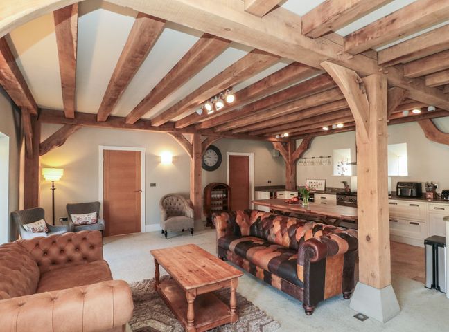 A living area with wooden beams sofas a wooden coffee table and a kitchen space at The Barn Helperby near Boroughbridge