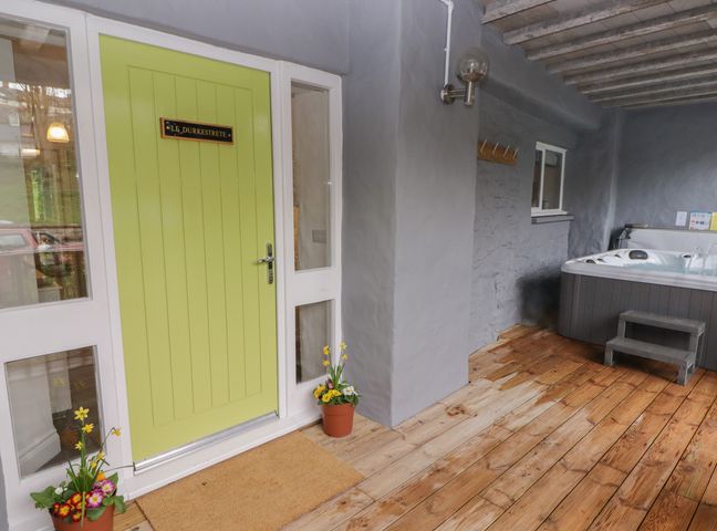 A covered outdoor area with a green door, two flower pots, wooden floor, and a hot tub at Le Durkestrete Cellar in Haverfordwest