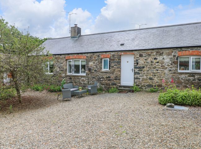 A stone cottage with three windows a white door a gravel yard and outdoor seating at The Stables Near Solva