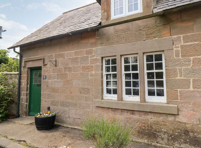 Exterior wall of a stone building with a green door and three white window panes and a flower pot on the ground at Cherry Tree Cottage in Fallodon near Embleton