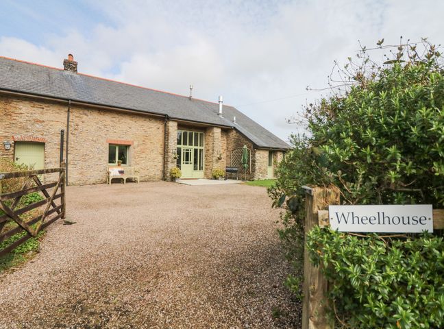 An exterior view of a stone house with a gravel driveway and a wooden gate at Wheelhouse in Muddiford near West Down