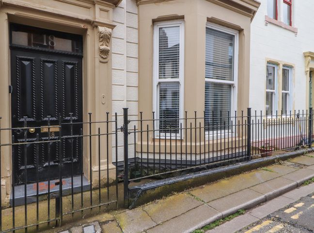 The exterior of a building with a black door numbered 18 and large windows behind a black metal fence