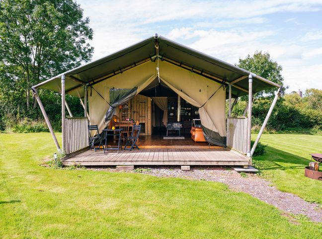 An outdoor tent with a wooden deck table and chairs surrounded by grass and trees at Oak Stockland near Dalwood