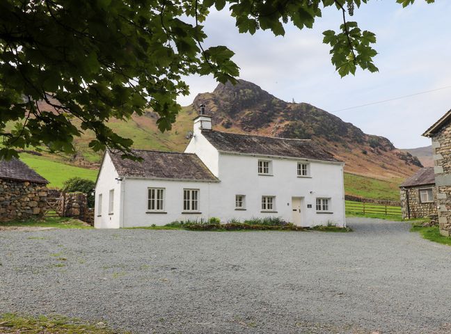 A white house with multiple windows and a gravel driveway in front with hills in the background at One Side House Farm in Langdale