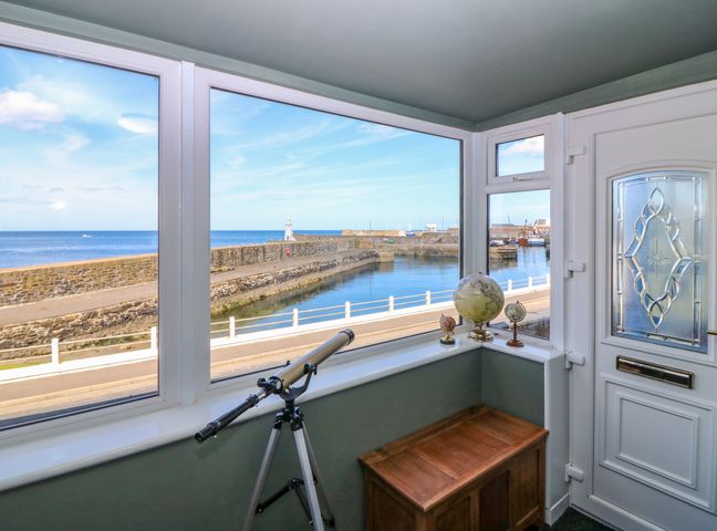 A corner with large windows overlooking a harbor with a telescope globes and a wooden chest at West Pier Cottage in Macduff