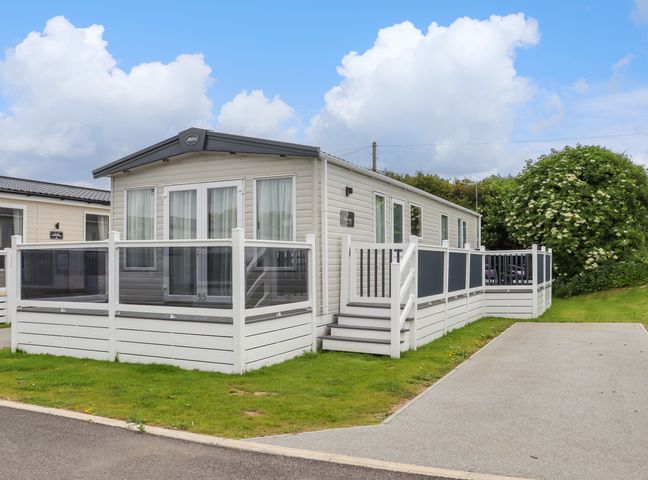 A white mobile home with a glass railing deck and steps on grass next to a paved driveway at Dollys Delight in Pevensey