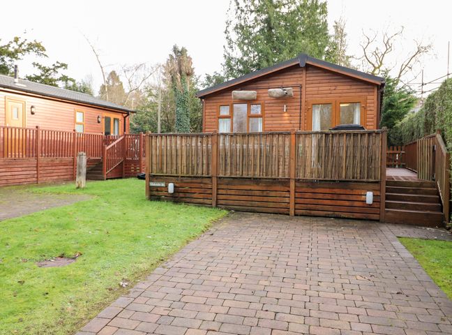 A wooden cabin with a fenced porch and paved driveway at Bowness Bay Lodge Oakside 16 Fallbarrow Park near Bowness-On-Windermere