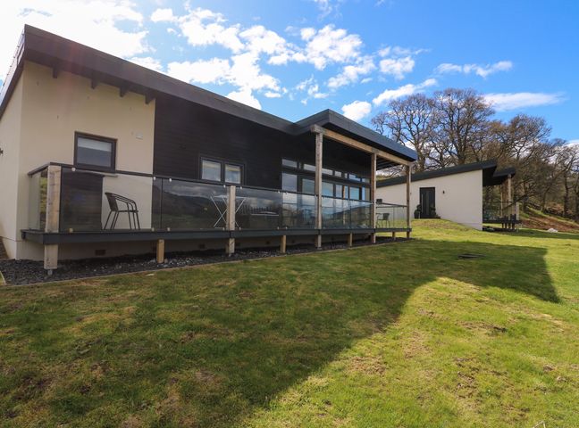 A modern lodge with a glass railing porch and chairs on a grassy lawn at 2 Strathtay Lodges in Aberfeldy