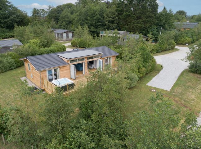 A wooden house with opened doors and a hot tub on the deck surrounded by trees at 5 Southern Place in Dobwalls