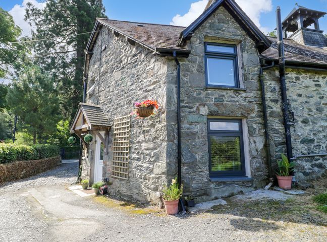 A stone cottage with two windows and a door with a small porch surrounded by plants at Y Bwthyn in Penmaenpool near Dolgellau