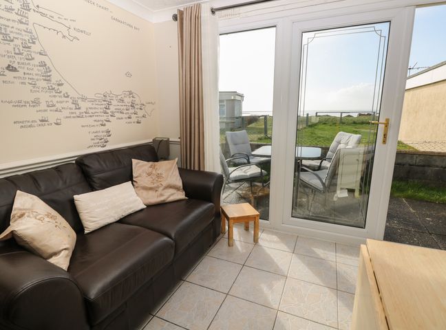 A living room with a black sofa with cushions and a wall map next to glass doors leading to an outdoor patio with chairs and a table at Shipwreck Chalet in Kidwelly