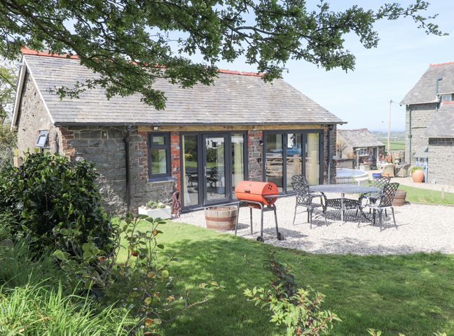 An outdoor patio area with a barbecue grill metal table and chairs in front of a stone house at Ael-y-bryn in Boduan near Tudweiliog