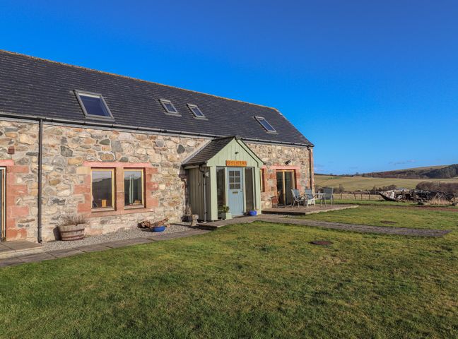 Stone barn with a green porch door and outdoor chairs on a grassy area at Reyflat Barn in Rosemarkie