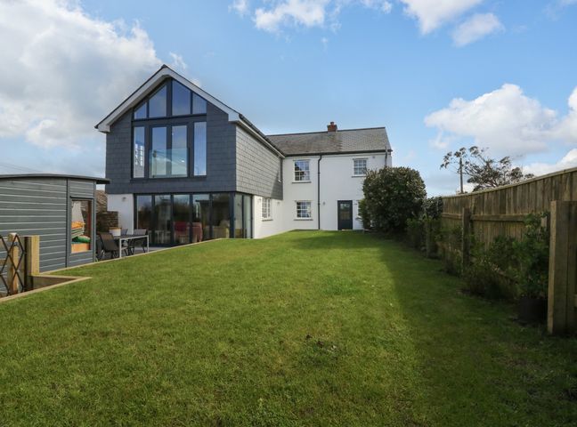 A backyard with grass a wooden fence a white house with large windows and a patio at Channel View House in Wadebridge