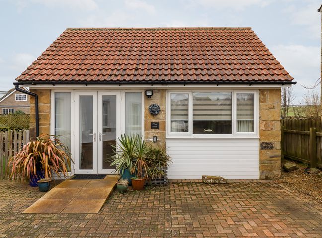 A single story building with a tiled roof two white doors and windows with plants in pots at The Nook in North Sunderland near Seahouses