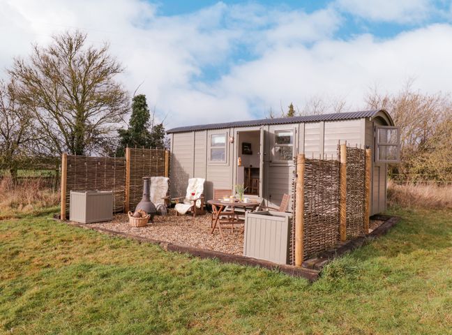 An outdoor seating area with wooden chairs and table near a small cabin with woven fences around it at Bumble's Retreat in Whepstead near Bury St Edmunds