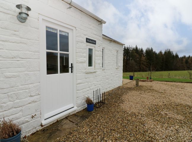Exterior view of a white stone building with a white door and windows a gravel area and grass field with trees at Woodland View Copley near Barnard Castle