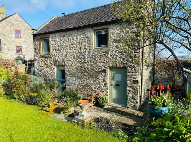 A stone house with a garden bench and red tulips in pots in front at Tor Barn in Winster