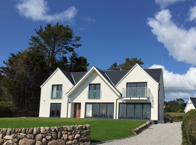 A modern two story house with balconies and large windows on a lawn with a stone wall and gravel driveway at Merse End in Rockcliffe near Dalbeattie