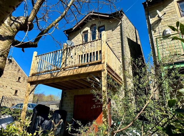The exterior of a stone house with a wooden balcony and garden furniture covered in black protective covers at The Squirrels in Hebden