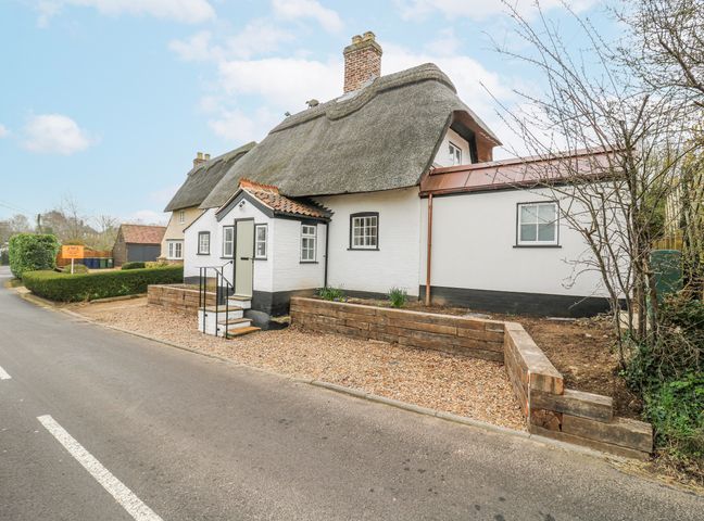 A cottage with a thatched roof and gravel pathway at The Old Smithy in Bourn