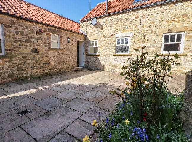 A stone courtyard with tiled roof buildings and a garden bed with flowers and plants at The Dairy in Ramshaw near Evenwood