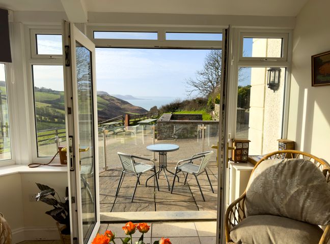 A patio with two metal chairs and a round table overlooking hills and water at Crogal Farmhouse in New Quay