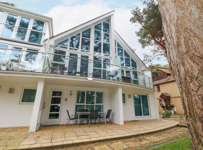 A modern two-story house with large triangular windows and a glass balcony railing at 5 Red Sails in Sandbanks