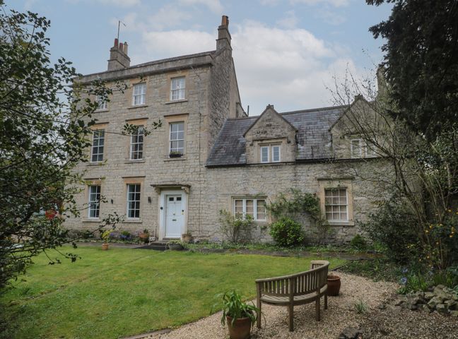 Stone house with white door and multiple windows surrounded by garden with grass trees and benches at Southbank in Bath