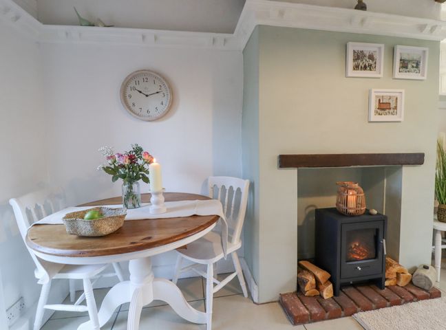 A dining area with a wooden table and white chairs next to a fireplace with a wood stove at Penny Cottage in Haworth