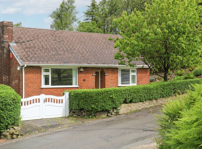 A brick house with white windows and a white gate behind hedges and trees at Belle Vue in Mow Cop