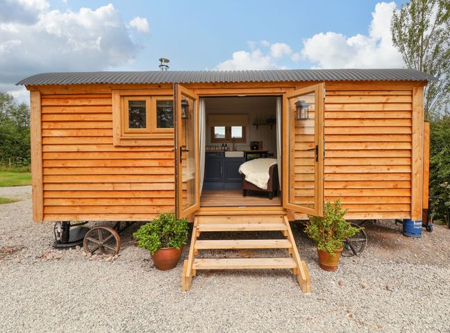 A wooden cabin with double doors open showing a chair and kitchen inside at Cariad Mawr in Gwaenysgor near Prestatyn