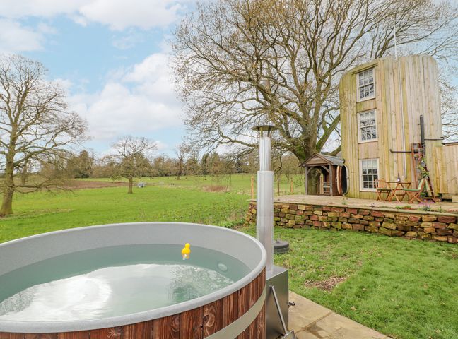 An outdoor hot tub with a yellow rubber duck near a wooden cylindrical building in a grassy field at The Lazy Squire by The Water Admaston near Rugeley