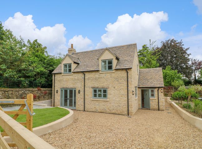 A stone house with blue framed windows and doors surrounded by gravel and garden at 9 Rectory Lane in Edith Weston