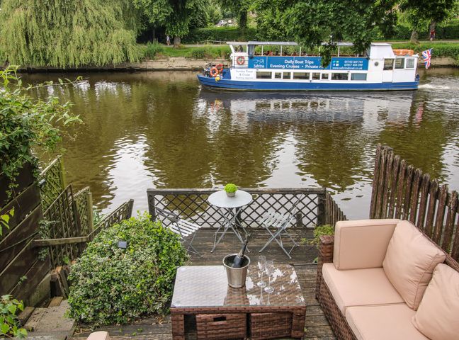 A riverside deck with outdoor seating and a boat on the river at Riverbank in Shrewsbury
