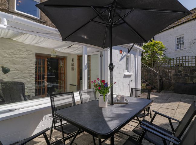 An outdoor patio with a black table and chairs under a black umbrella and a vase with flowers at 2Loos in Garlieston