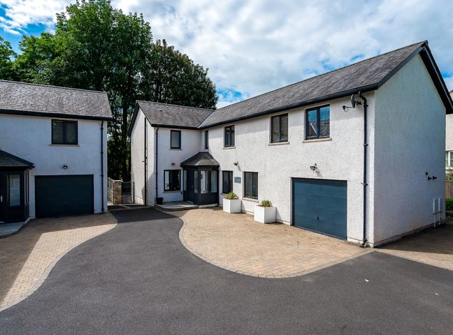 An exterior view of two white houses with driveways and garages surrounded by trees at Pen-y-Ghent in Kirkby Lonsdale