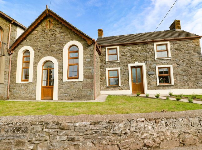 Stone cottage with wooden doors and windows and a grass lawn at Dalton Cottage in Llansaint